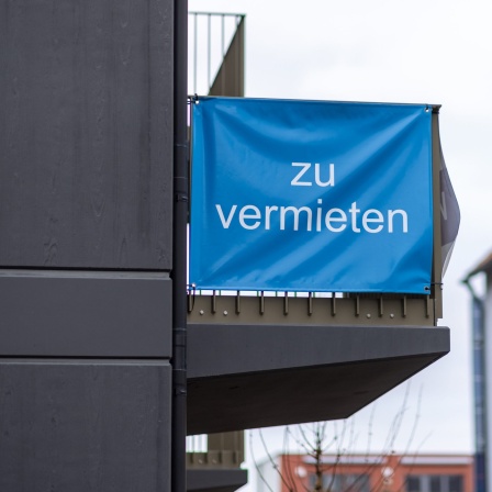 "Zu vermieten" steht auf einer Plane, die an einem Balkon-Geländer einer Neubau-Wohnung angebracht ist.