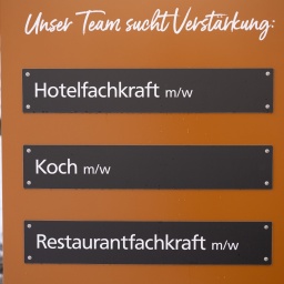 Ein Schild wirbt neben einem Hotel für freien Stellen für die Bereiche Hotelfachkraft; Koch und Restaurantfachkraft.