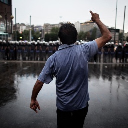 Ein gestikulierender Mann steht auf dem Taksim-Platz einer Reihe schwer uniformierter und bewaffneter Polizisten gegenüber. Man sieht die Person von hinten.