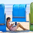 Eine Frau mit Laptop und Mobiltelefon am Strand, zwischen Strandkörben.