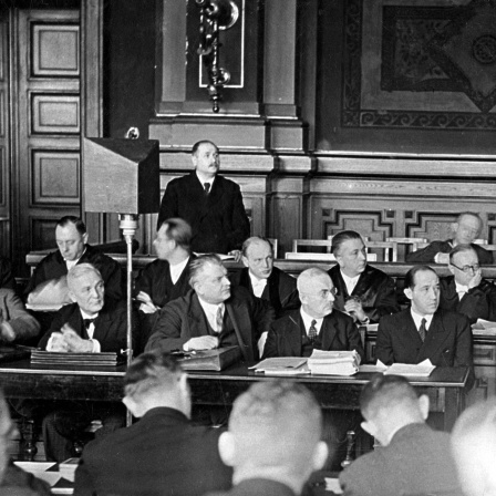 Die führenden Männer des Reichsrundfunks wurden, soweit sie als NS-Gegner bekannt waren, nach der Machtergreifung verhaftet und am 5. November 1933 vor Gericht gestellt. Staatssekretär Dr. Hans Bredow (stehend) während seiner Aussage, rechts von ihm sitzend Dr. Kurt Magnus, Direktor der Reichsrundfunkgesellschaft. 2. Reihe die Verteidiger und in der vorderen Reihe die weiteren Angeschuldigten von links: Zorek, Korte, Dr. Jaeger, Dr. Kohl, Dr. Otto und Intendant Flesch.