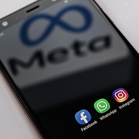 Auf einem Smartphone sind die Apps von Facebook, Whatsapp und Instagram zu sehen. Auf dem Bildschirm spiegelt sich der Schriftzug plus Logo von Meta.