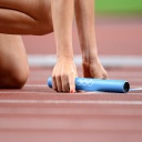 Eine Leichtathletin hält beim 4x400 Meter Staffellauf den Staffelstab beim Start in der rechten Hand.