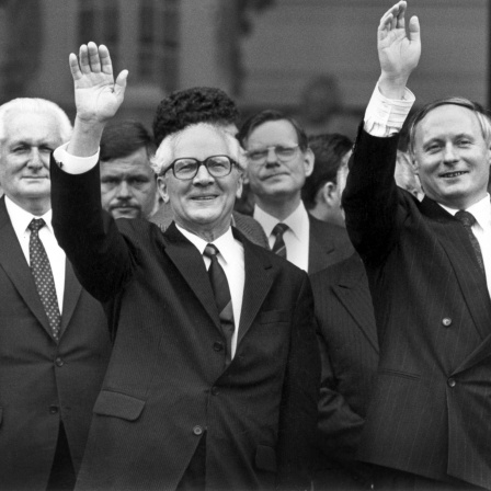 Geinsam winken der saarländische Ministerpräsident Oskar Lafontaine (rechts) und sein Gast, der DDR-Staatsratsvorsitzende und SED-Chef Erich Honecker (Mitte) nach der Besichtigung der barocken Ludwigskirche am 10.9.1987 in Saarbrücken den rund 100 Zuschauerrn zu. Links steht Honeckers Stellvertreter Günter Mittag.