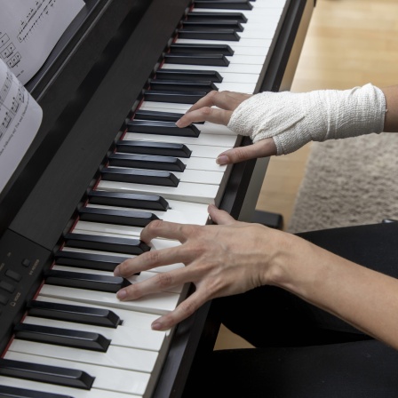 Symbolbild Sehnenscheidenentzündung: Frau mit Handgelenkbandage am Klavier