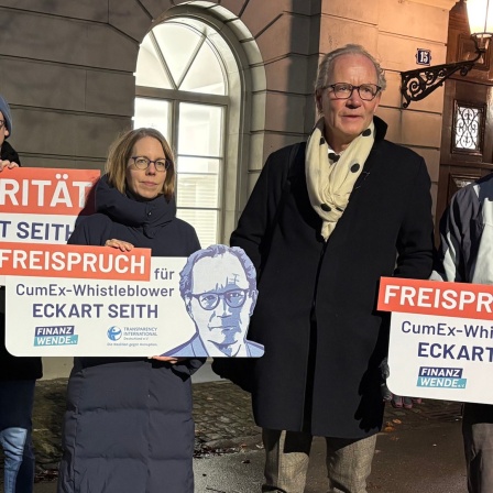 Rechtsanwalt Eckart Seith (2.v.r.) neben der ehemaligen Chefermittlerin im Cum-Ex-Komplex, Anne Brorhilker (M). Daneben Demonstraten, die Schilder mit der Aufschrift: "Freispruch für CumEx-Whistleblower Eckart Seith" und "Solidarität mit Eckart Seith" tragen