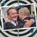 Eine Bildmontage zeigt eine Dartscheibe. Darauf ist eine Postkarte zu sehen. Sie zeigt Ex-Bundeskanzler Gerhard Schröder, der Wladimir Putin herzlich umarmt.