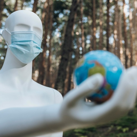 Ein Roboter mit medizinischer Maske hält eine Weltkugel in seiner Hand (Bild: picture alliance/Westend61/Jose Carlos Ichiro)