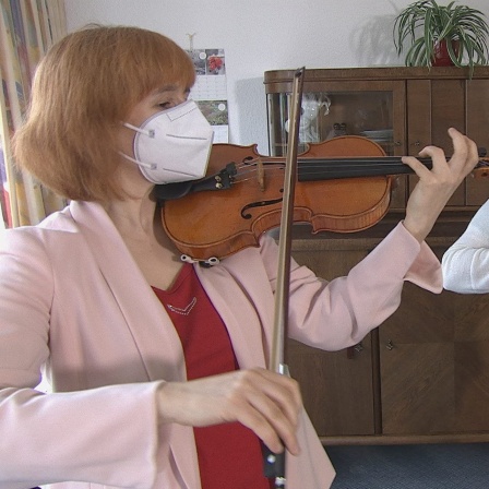 Eine Geigenspielerin und eine Frau mit Akkordeon spielen Musik im Pflegeheim. Beide tragen einen mit Mundnasenschutz.