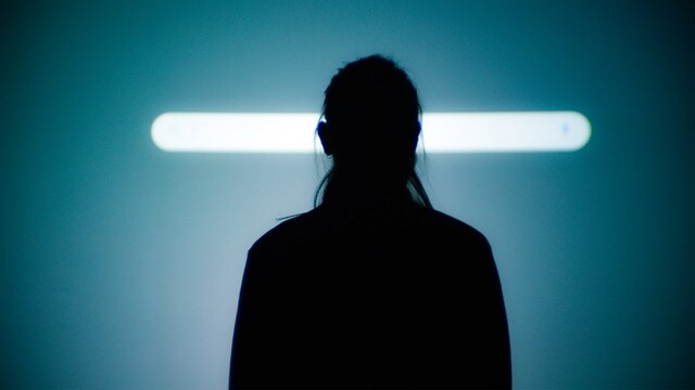 Schattenriss einer Frau vor einer länglichen Lichtleiste.