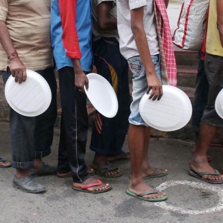 Menschen in ärmlicher Kleidung mit Tellern in der Hand warten auf eine Essensausgabe in Kalkutta (Indien), inmitten der Covid-19 Pandemie, 27. August 2020. 