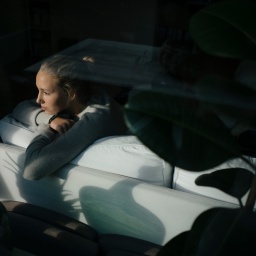 Eine Jugendliche sitzt auf dem Sofa und guckt aus dem Fenster.