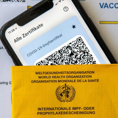 Ein Impfpass und ein Smartphone, auf dem die App CovPass läuft