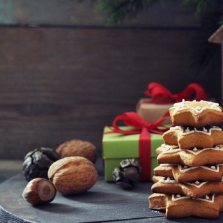 Weihnachtskekse und Nüsse liegen gestapelt vor einem Windlicht aus Holz.