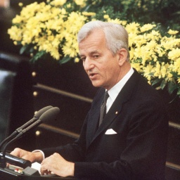 Der deutsche Bundespräsident Richard von Weizsäcker bei seiner vielbeachteten Rede im Bonner Bundestag am 8.5.1985 während der Feierstunde zum Ende des 2. Weltkrieges. Er steht im schwarzen Anzug vor einem gelben Blumenbouquet am Mikrofon.
