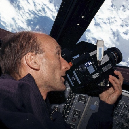 Ein Mann schaut durch eine Kamera aus dem Space Shuttle ins Weltall. Es ist der deutsche Astronaut Gerhard Thiele.
