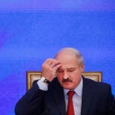 Der belarussische Präsident Lukaschenko sitzt neben einer Flagge und schaut zu Boden, dabei kratzt er sich am Kopf