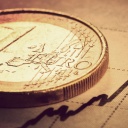 Eine Euro-Münze liegt auf einem Blatt Papier mit aufgemalten Kurven. 