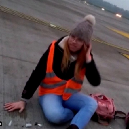 Eine junge Frau, die auf dem Boden einer Startbahn an einem Flughafen sitzt