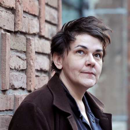 Die Sängerin Christiane Rösinger steht vor einer Backsteinmauer.