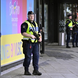 Polizisten stehen vor der Malmö-Arena, an der das Logo vom ESC zu sehen ist.