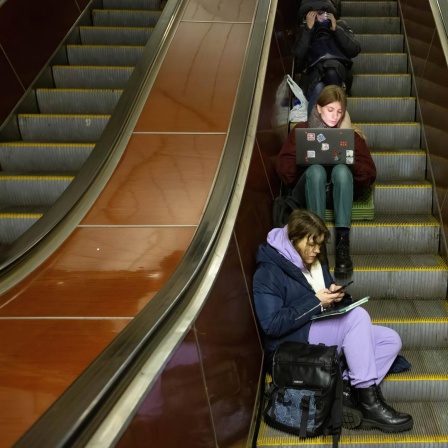 Junge Menschen mit Smartphone und Laptop sitzen auf einer Rolltreppe in einer U-Bahn Station in Kiew und warten einen Luftangriffalarm ab. 13. Dezember 2022, Kiew, Ukraine.