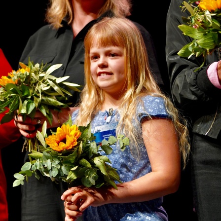 Ein Mädchen steht auf einer Bühne, es hält einen Blumenstrauß in der Hand