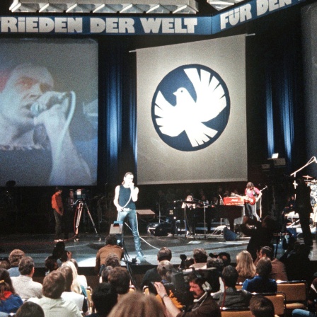 Udo Lindenberg 1983 auf der Bühne im Ostberliner Palast der Republik, darüber ein Banner mit dem Spruch "Für den Frieden der Welt"