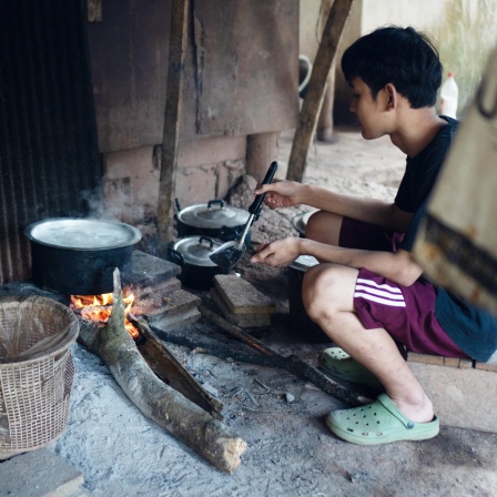 Ein Junge, der mit seiner Familie vor den Angriffen der Militärjunta geflohen ist, kocht Reis in einem Vertriebenencamp im Dschungel an der Grenze zu Thailand. Sauberes Trinkwasser gibt es nicht, Lebensmittel sind knapp. 16.01.2023.