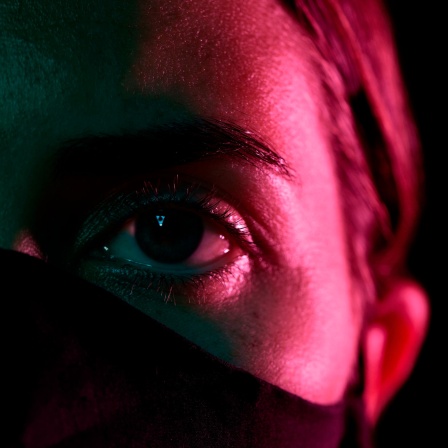 Eine Frau trägt eine schwarze Maske, nur ihre Augen sind zu sehen.