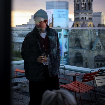 Lars Eidingers Spiegelung in einem Fenster auf einer Dachterrasse.