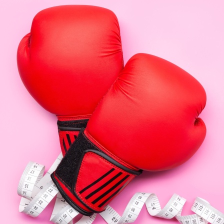 Ein Paar Boxhandschuhe und ein Maßband vor rosa Hintergrund
