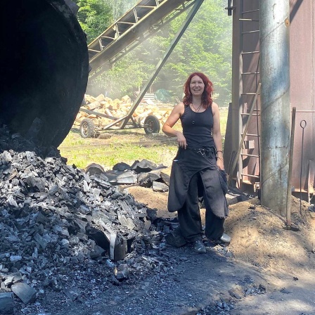 Eine Frau steht neben einem Berg Holzkohle