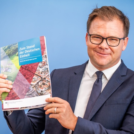 Carsten Schneider (SPD), Staatsminister und Ostbeauftragter der Bundesregierung, zeigt den Bericht zum Stand der Deutschen Einheit