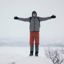 Ein glücklicher Mann in warmen Kleidern steht mit ausgestreckten Armen auf verschneitem Terrain in Finnland.