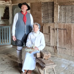 Ein älteres Paar in historischer Kleidung befindet sich in einem Hühnerstall.