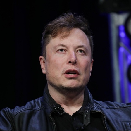Oberkörperporträt von Elon Musk. Er trägt ein schwarze Jacke und darunter ein ebenfalls schwarzes Oberteil. 