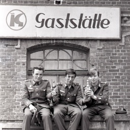 Wehrsoldaten der Nationalen Volksarmee sitzen vor einer Konsum Gaststätte.