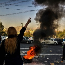 Frau vor brennendem Autoreifen im Iran mit gebobener Hand