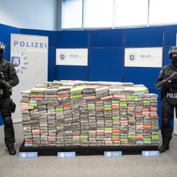Bewaffnete Polizeibeamte stehen neben sichergestellten Kokainpaketen.