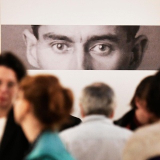 Eine Fotografie von Kafkas Augenpartie starrt Leute in einer Galerie an.