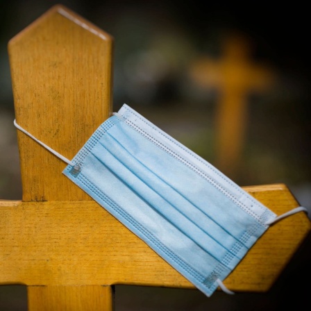 Eine Mundschutzmaske hängt an einem Grabkreuz