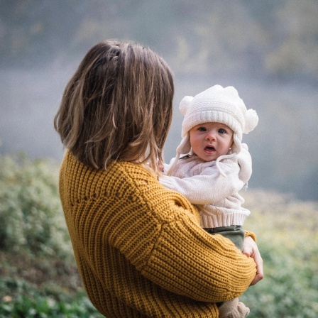 Baby auf dem Arm seiner Mutter vor einem See im Hintergrund