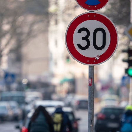Auto- und Radfahrer passieren ein Verkehrschild in einer Zone mit 30 Kilometern Geschwindigkeitsbeschränkung