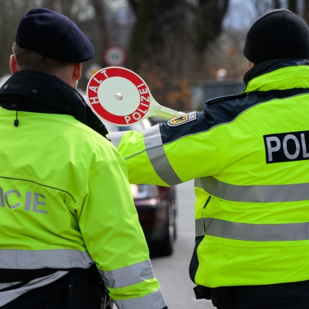 Ein Polizist aus Tschechien und ein Bundespolizist winken nahe dem Dreiländereck von Deutschland, Polen und Tschechien ein Auto zu Kontrolle heraus.