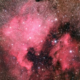 Stark vergrößert sind rot glühende Gaswolken und dunkle Staubwolken am Himmel zu sehen. Sie haben die Form von Nordamerika.