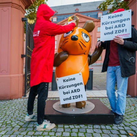 Mainz: Die Figur der Maus aus der "Sendung mit der Maus" steht zwischen Aktivisten von Campact vor dem Landtag Rheinland-Pfalz, die Schilder mit der Aufschrift "Keine Kürzungen bei ARD und ZDF!" halten. 