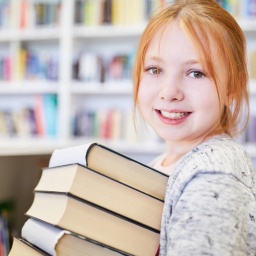 Ein lächelndes Mädchen trägt einen Stapel Bücher.
