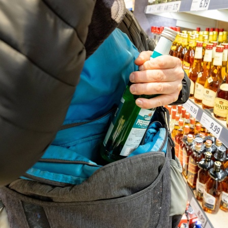 Ein Mann steckt eine Flasche Alkohol in seine Jacke.