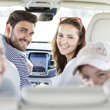 Auf dem Bild ist eine vierköpfige Familie zu sehen, die in einem Auto sitzt und in die Kamera lächelt.
